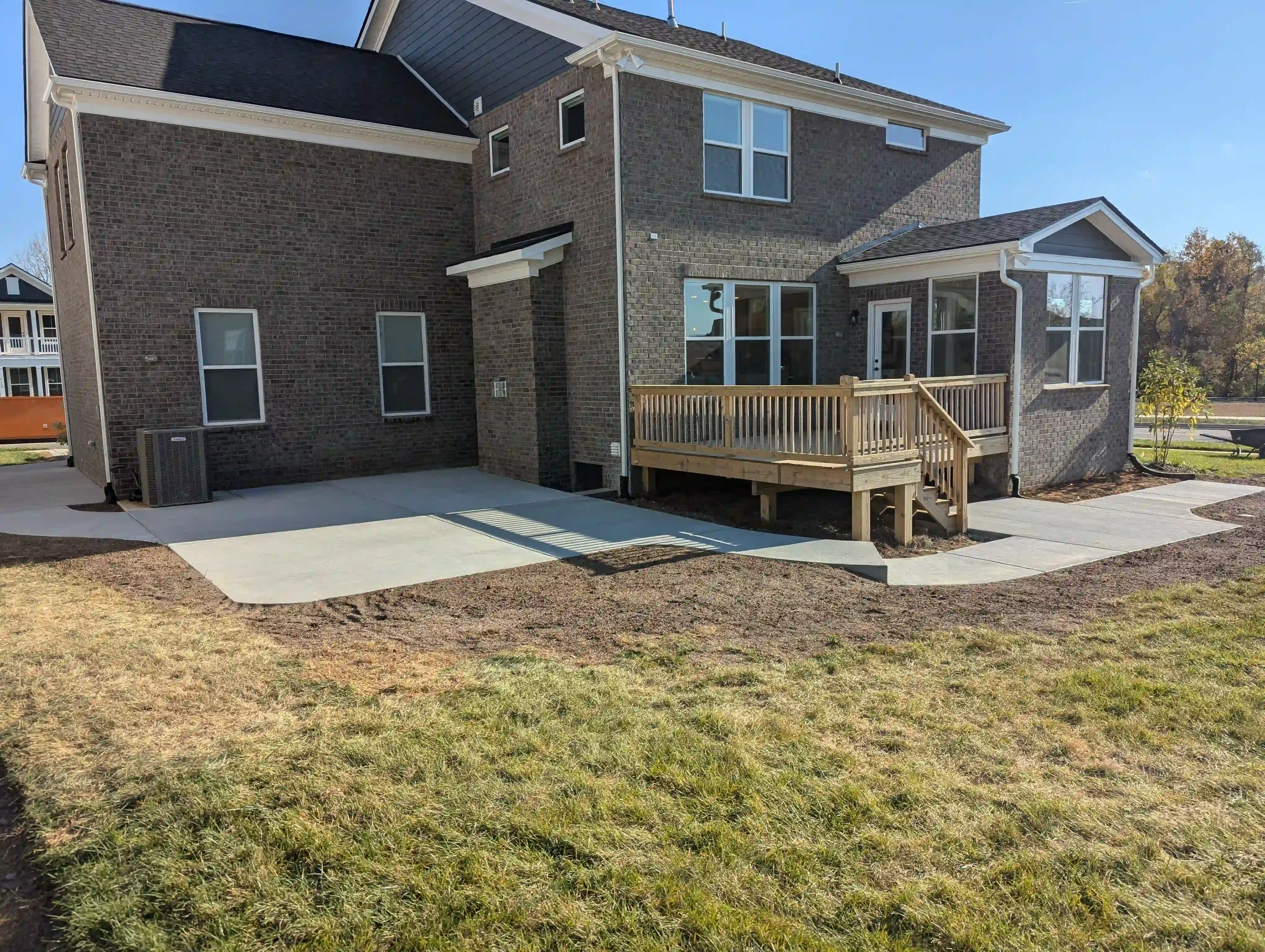 two concrete pads in the backyard of a home connected by a concrete sidewalk with a step
