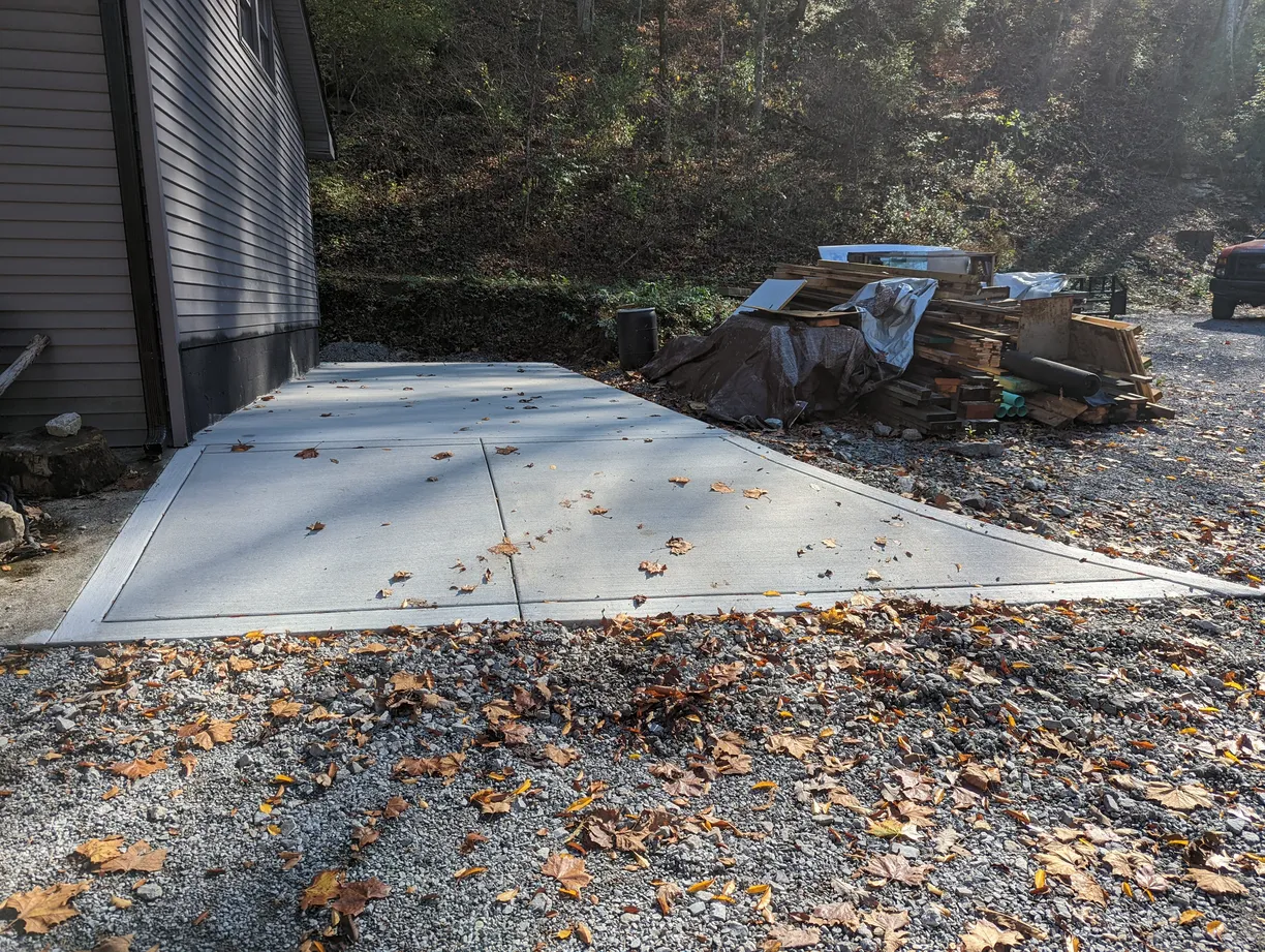 leaves on a gravel driveway leading to a concrete parking spot