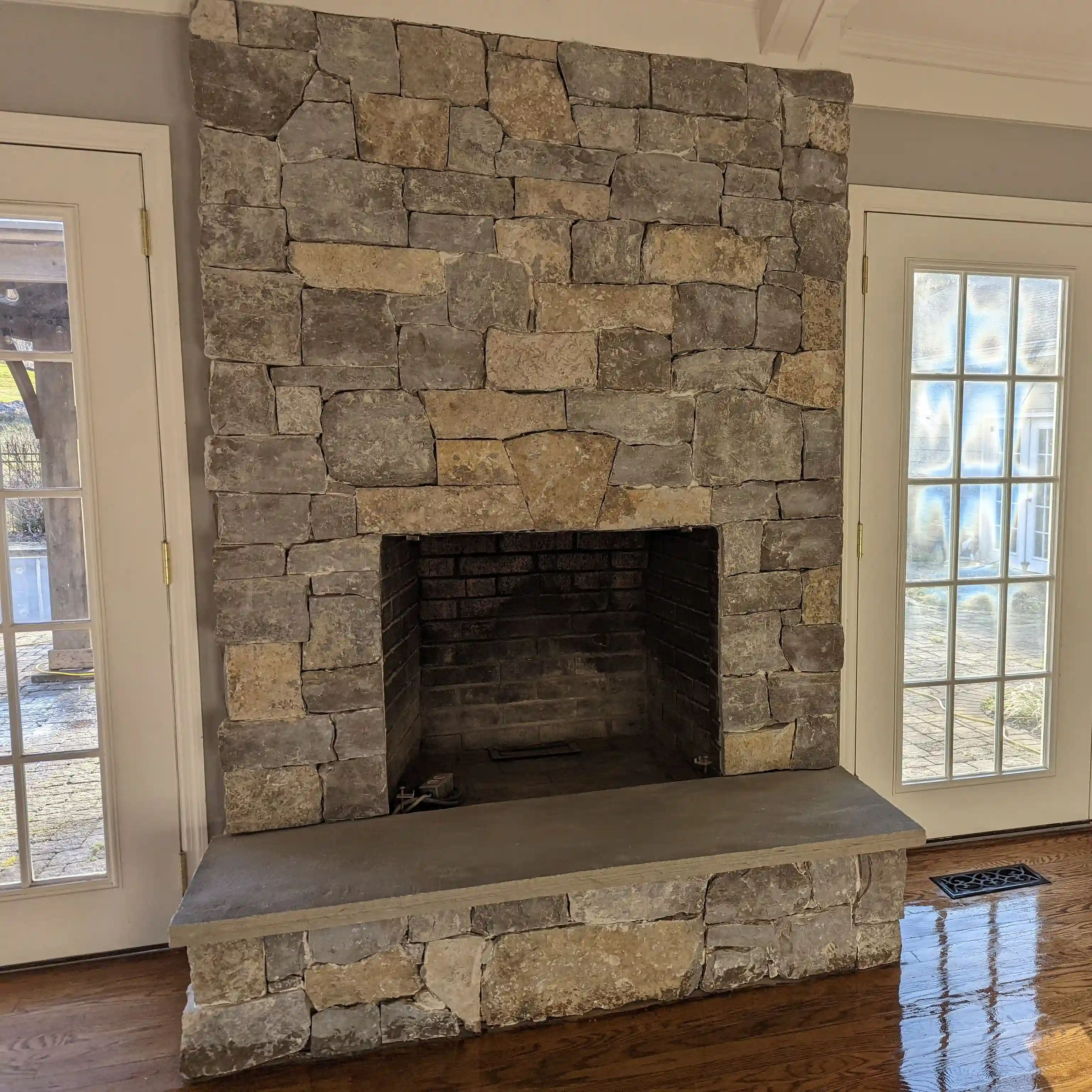 indoor stone fireplace with white doors on either side and a hardwood floor