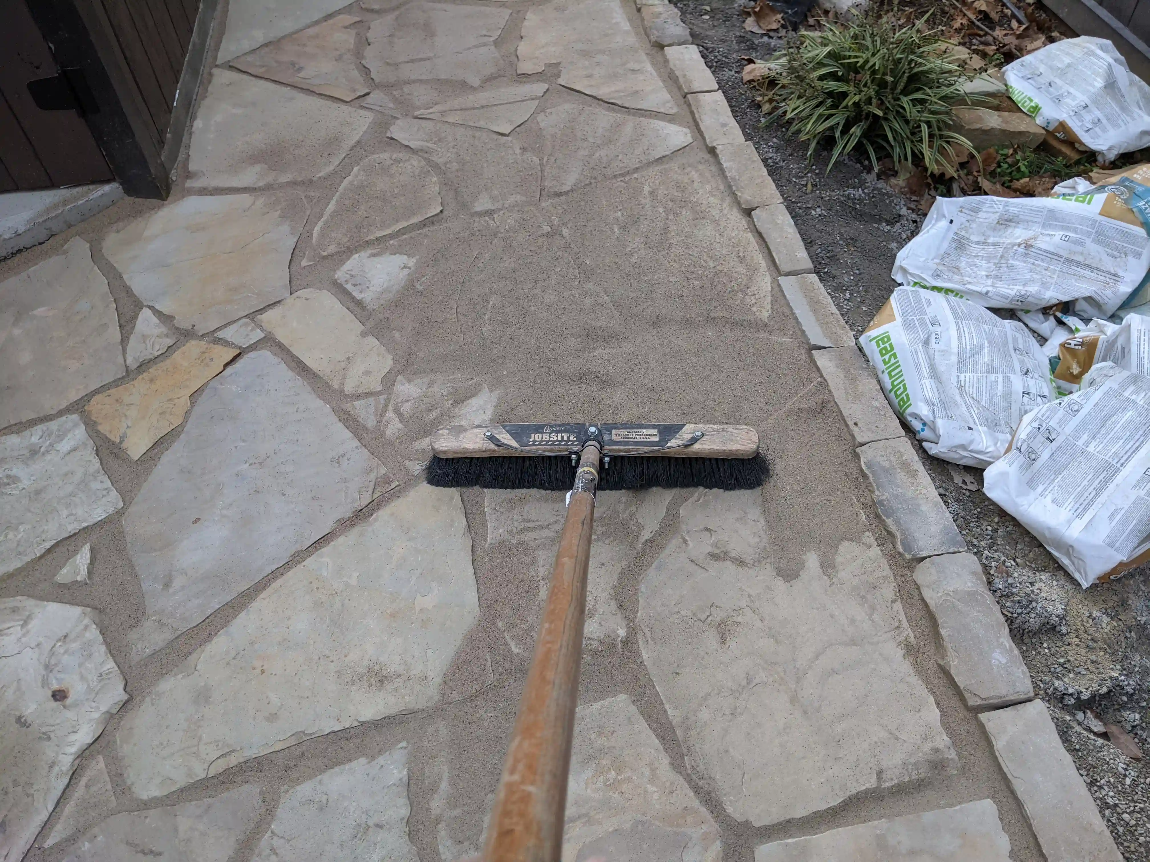 a push broom being used to fill in the gaps of a flagstone pathway with dirt