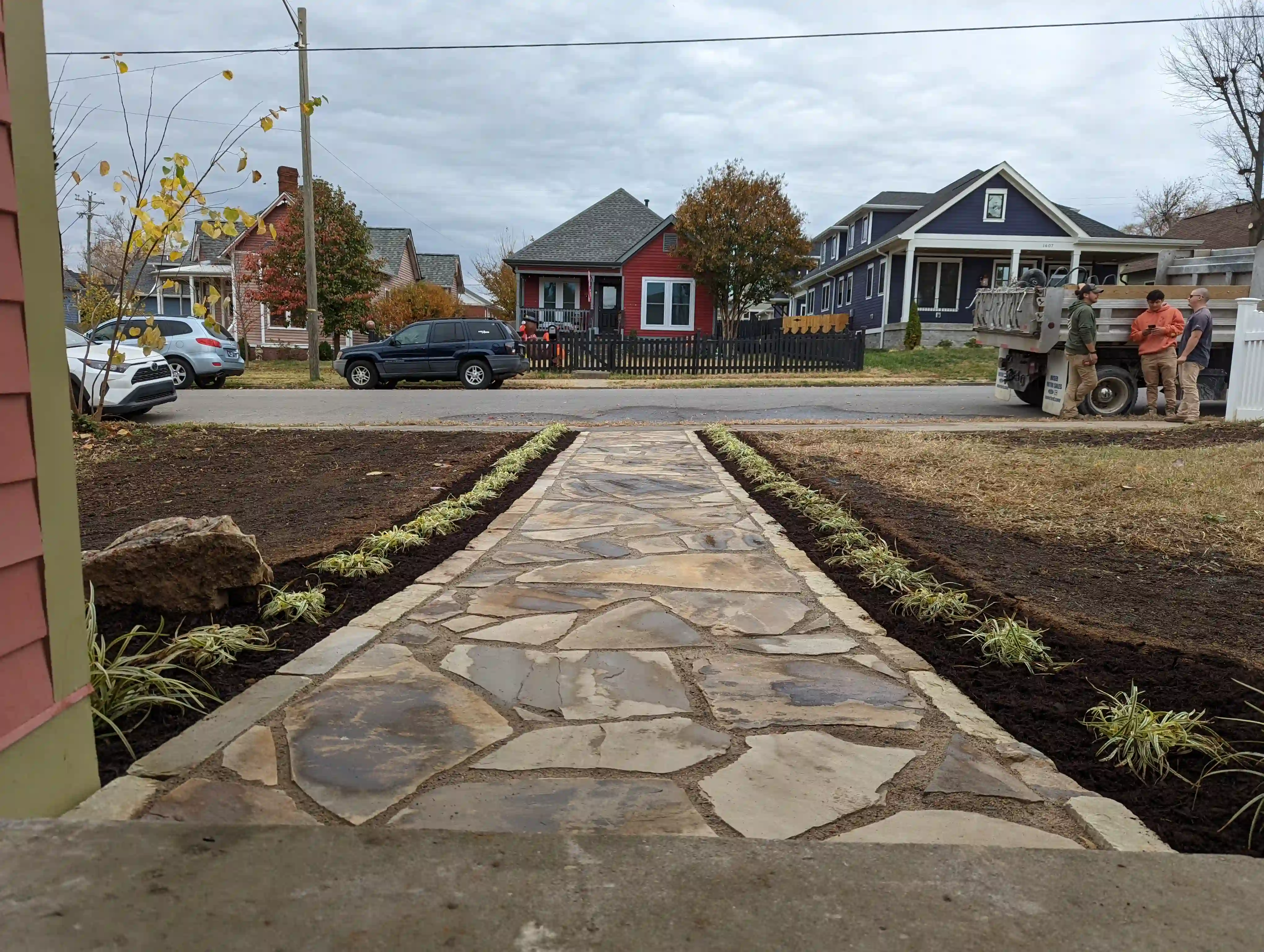 a finished flagstone walkway that ends at a sidewalk. the walkway is lined with garden beds on either side with small green shrubs