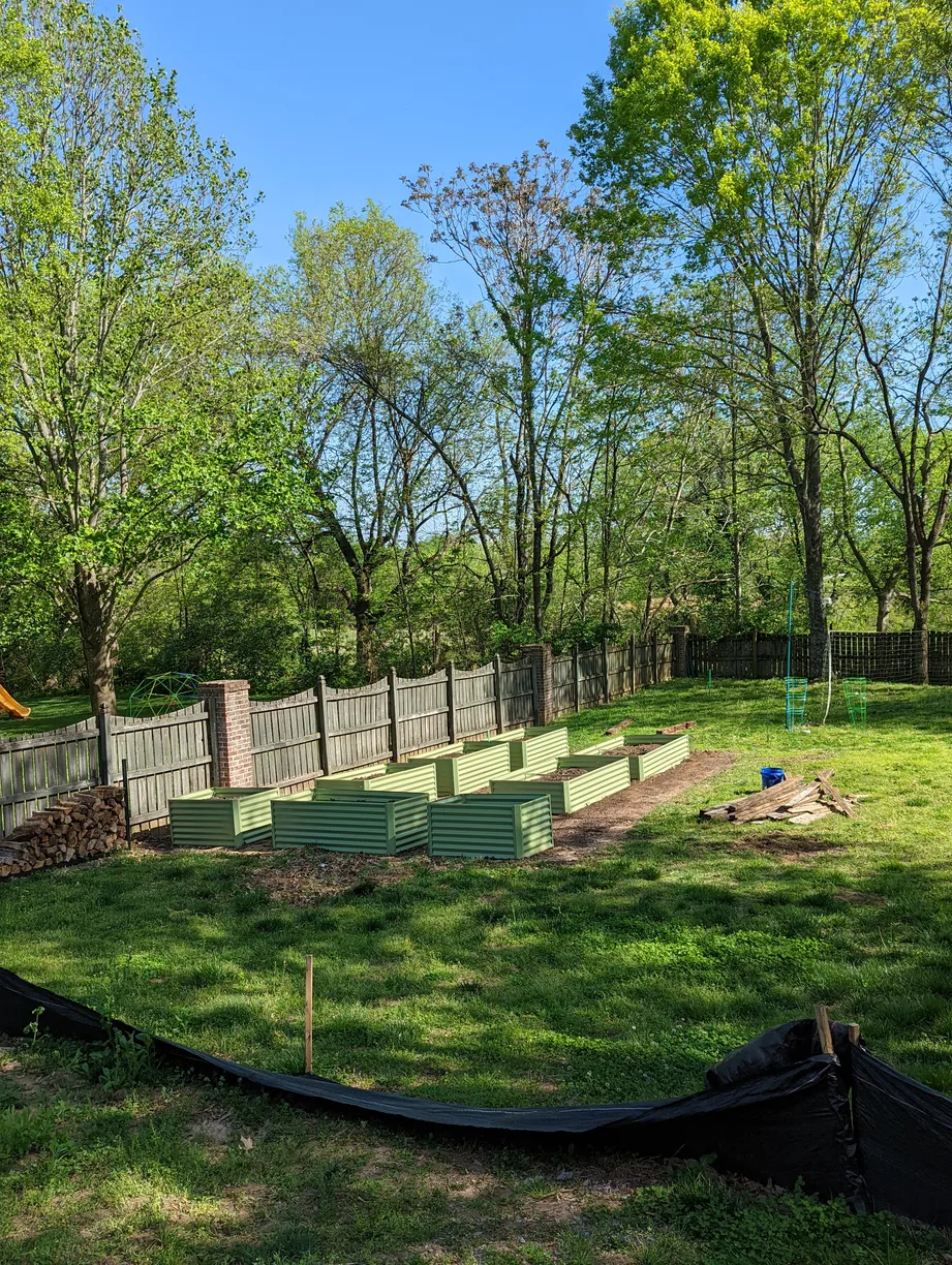 a suburban backyard lined with a wooden fence and has 8 green planter beds