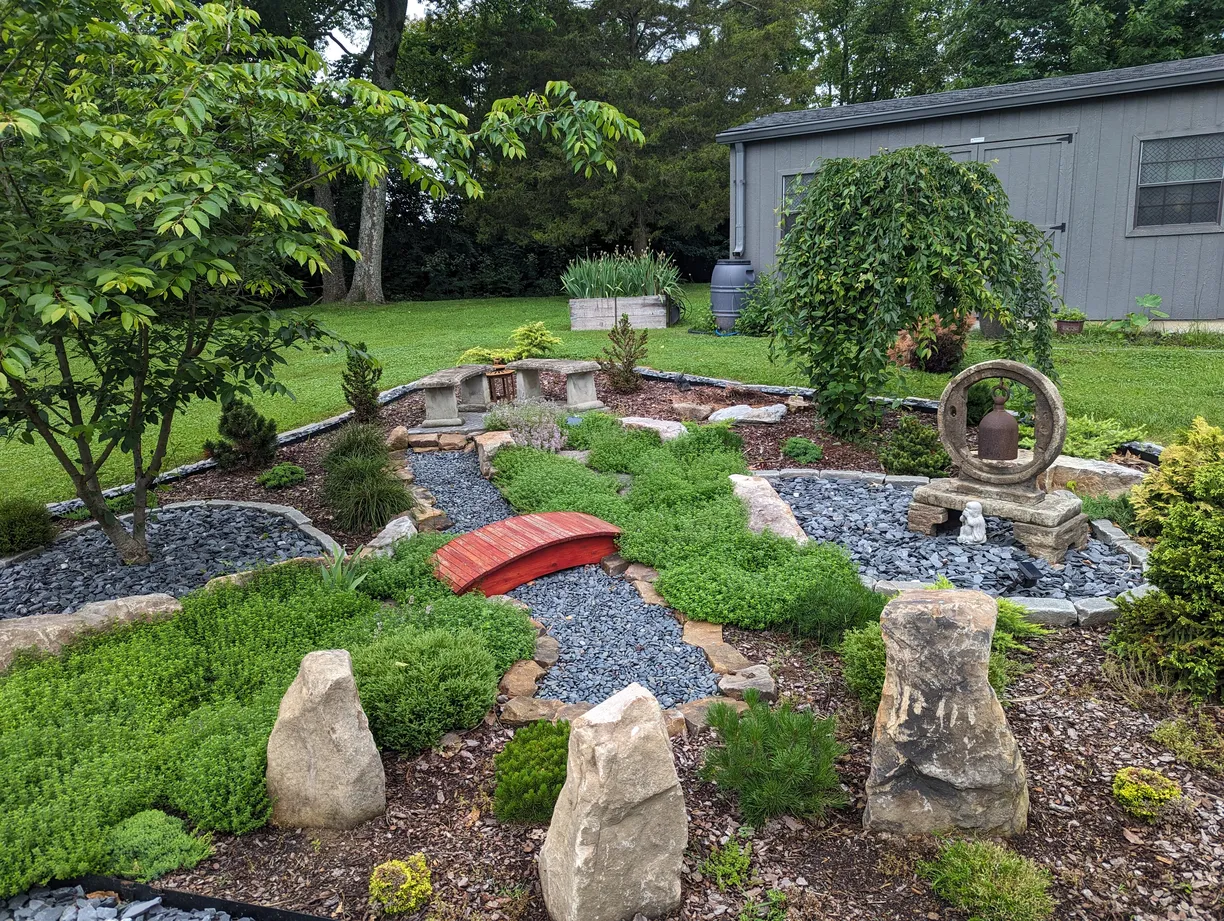 wonderful zen garden with a lot of green areas, gravel areas, large stones, a few stone benches and a small red bridge