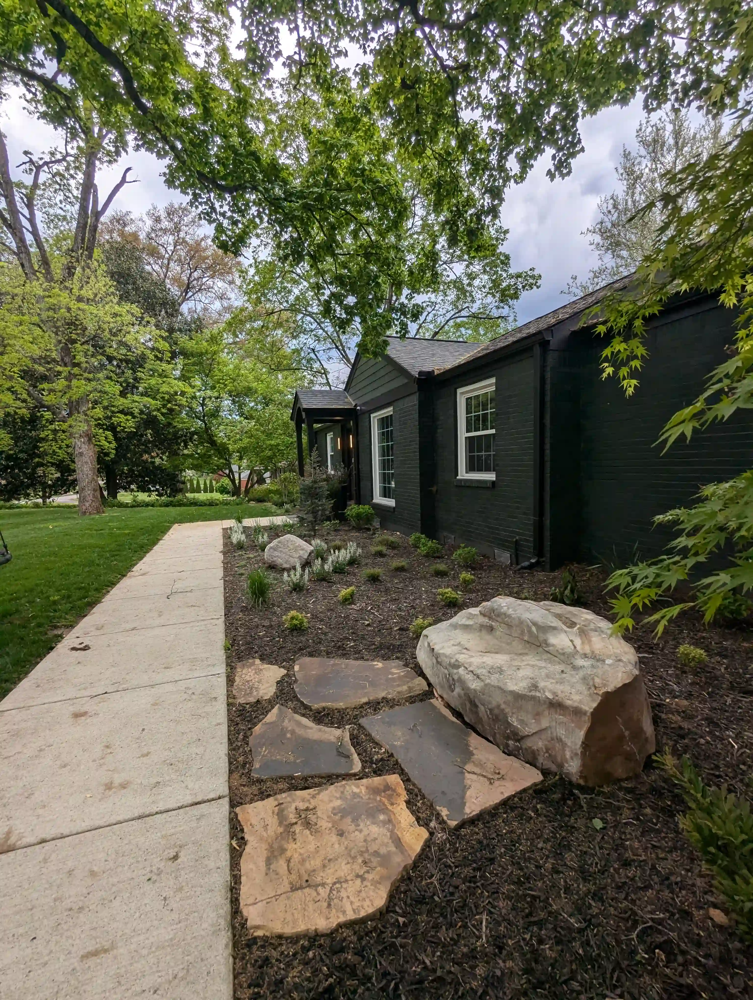 large boulder in a foundation bed outside of a black brick house