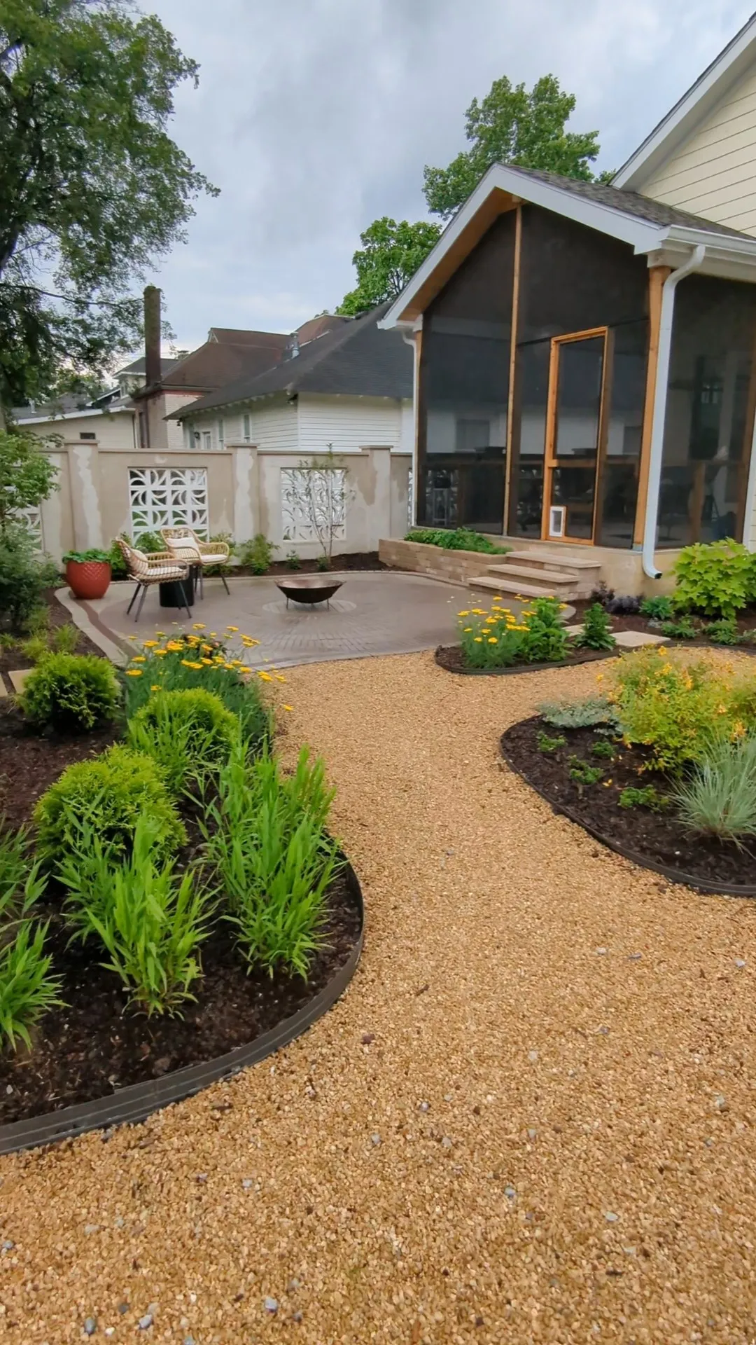 concrete patio outside of a screened in porch surrounded by garden beds with plants