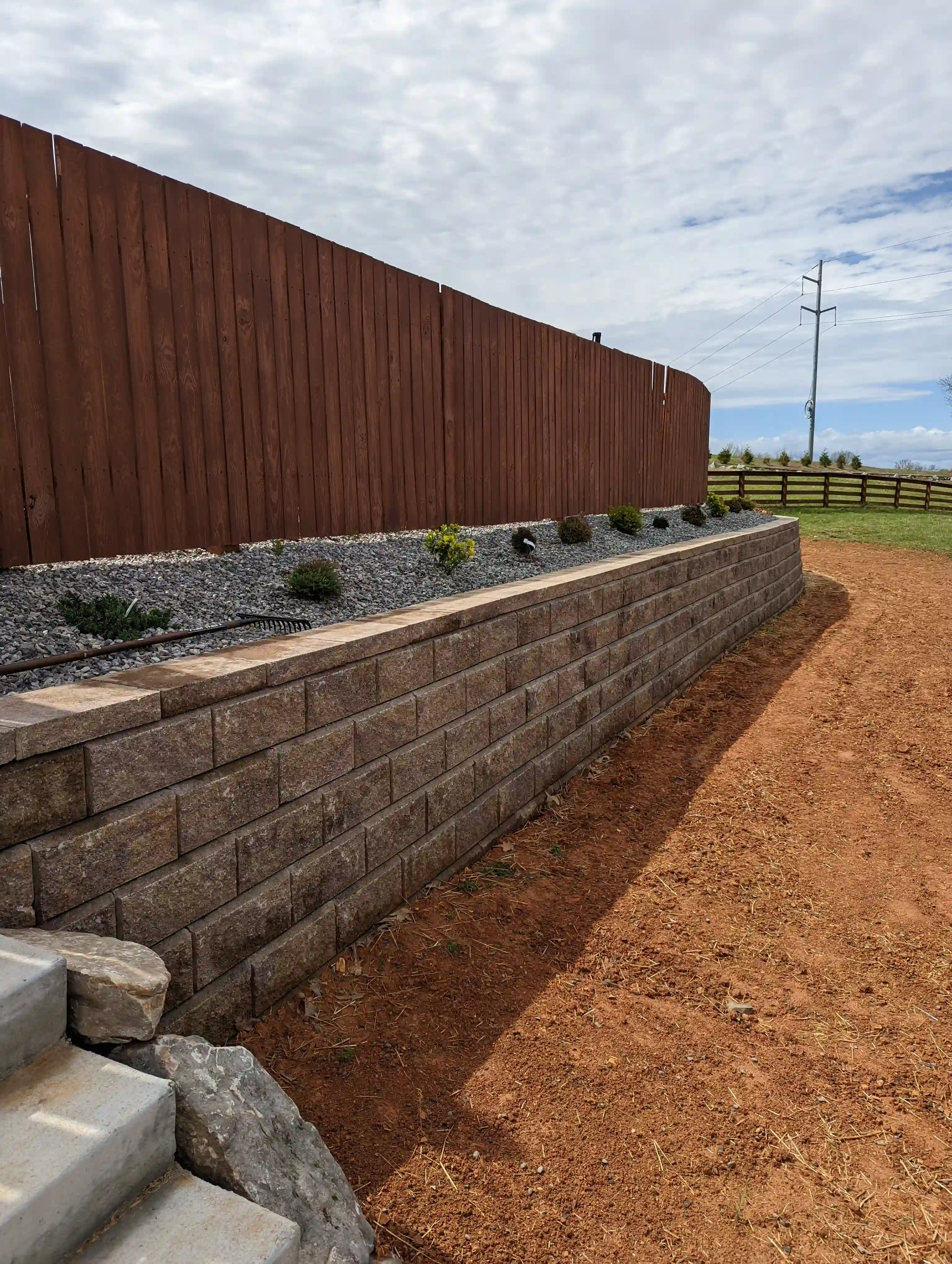 square stone retaining wall holding up a small gravel bed and fence