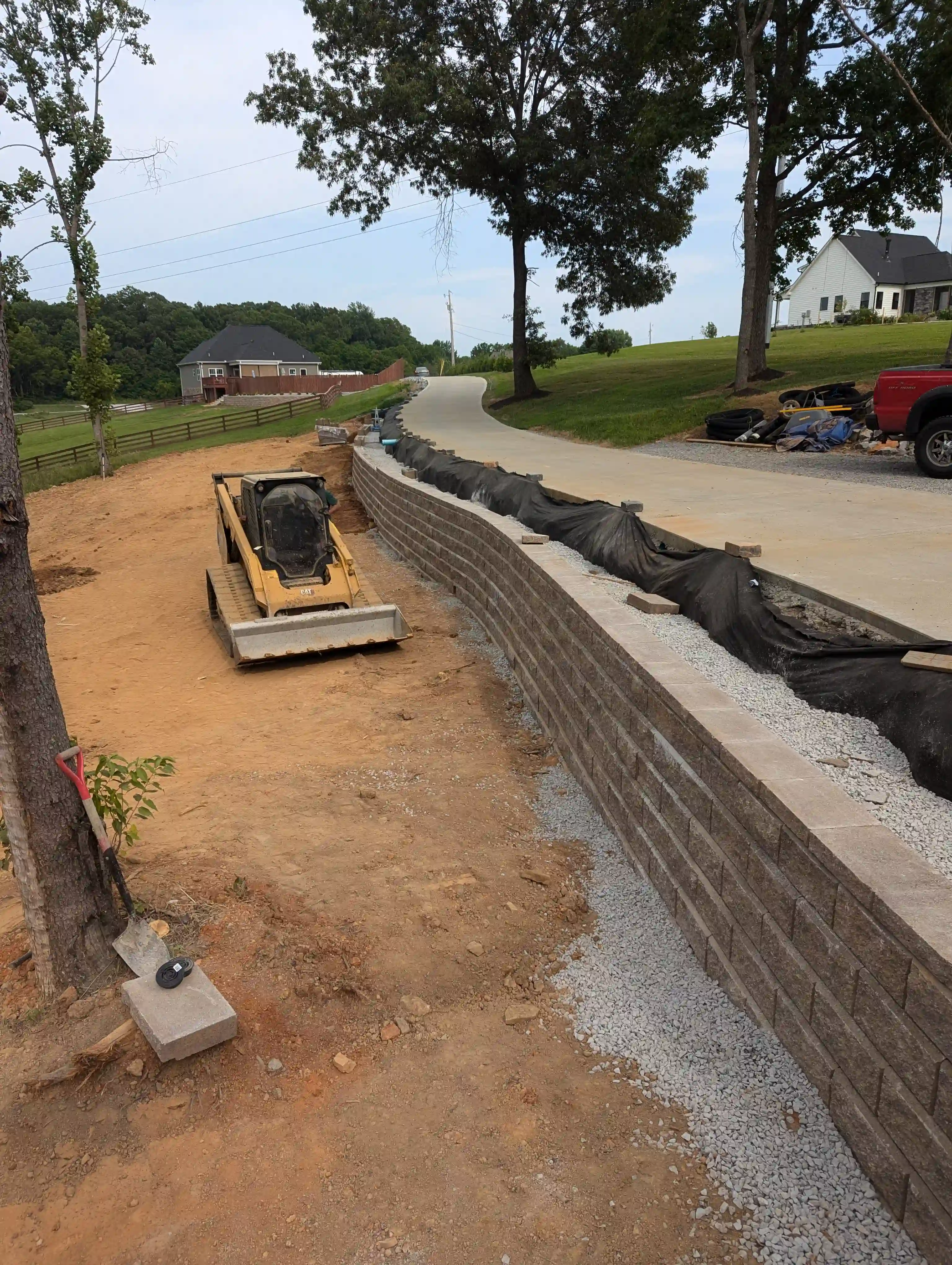 bulldozer in dirt next to a large retaining wall holding up a driveway