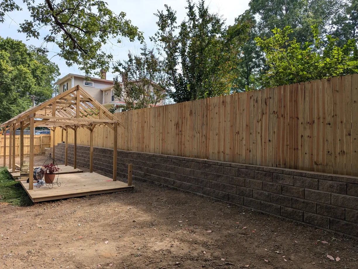 retaining wall build holding up a fence with a concrete pad and framed building