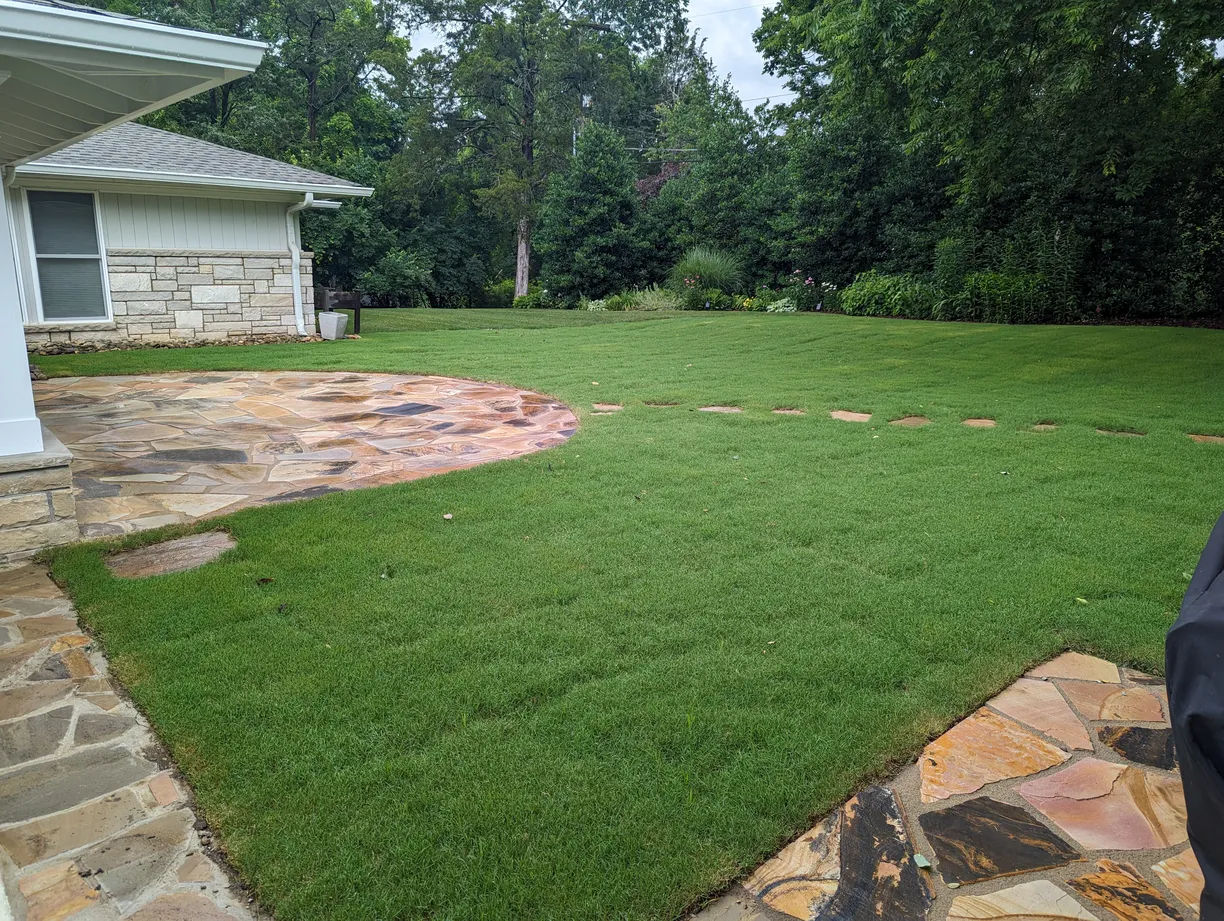 a backyard with a flagstone patio and freshly installed sod grass
