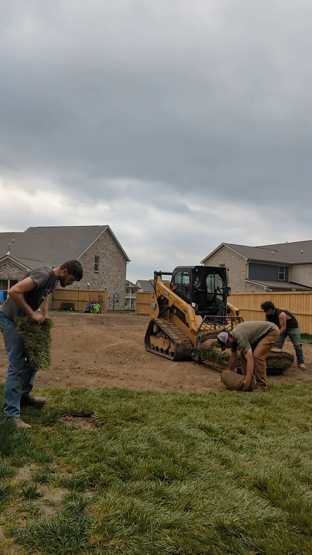 workers next to a forklift laying sod down in a suburban backyard
