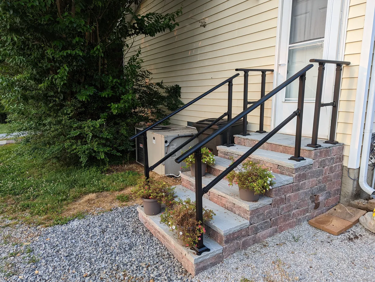 the exterior of a home with red brick stairs leading to the back door. the stairs have black rails and potted plants on every other step